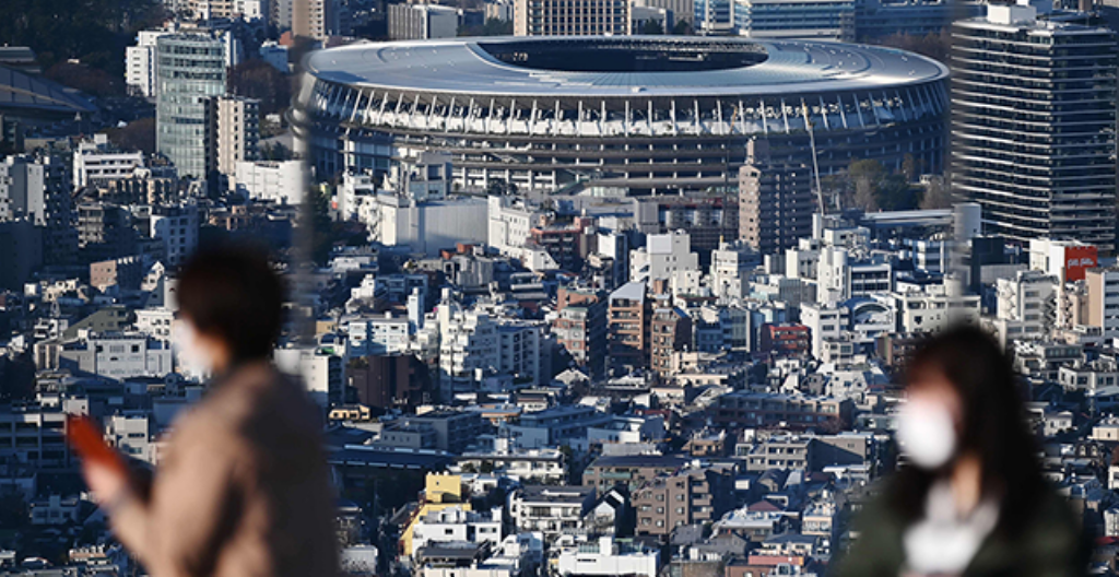 Kuvassa on Tokion olympiastadion ja pariskunta, joka käyttää hengityssuojaimia. Kuva on otettu 25. maaliskuuta.