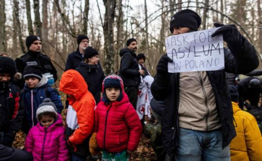 Kuvassa on Puolan rajalla perhe, joka on lähtenyt Kurdistanista. Perhe pääsi Puolan puolelle, mutta heidät palautettiin Valko-Venäjälle. Miehen kädessä on paperi, jossa lukee: ”Anon turvapaikkaa Puolasta.”