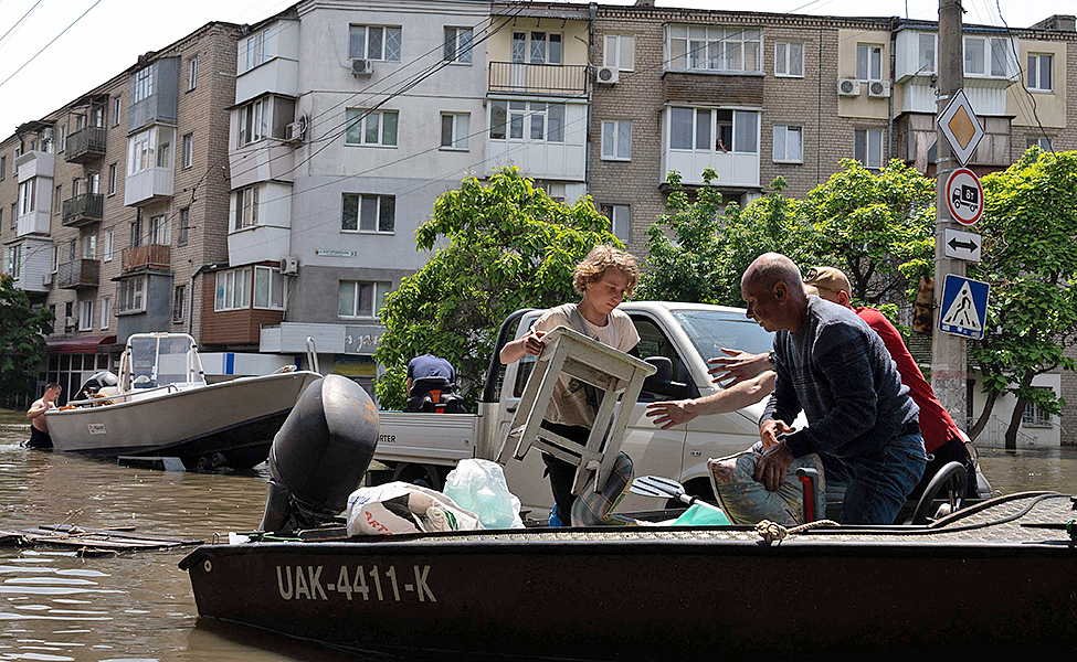 Vettä tulvii Etelä-Ukrainassa Khersonin kaupungin kaduilla. Nuori mies lastaa tavaroita veneeseen, ja kaksi muuta miestä ottavat tavaroita vastaan.