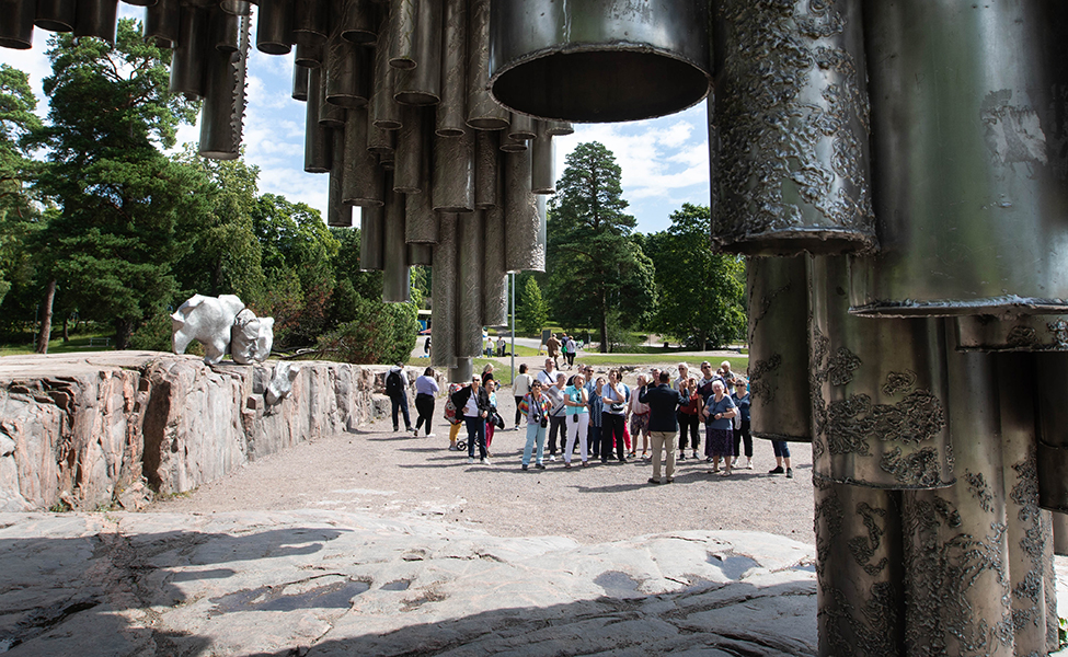 Etualalla yläreunaa kehystää Sibelius-monumentin putket. Kuva on otettu monumentin eli veistoksen alapuolelta ja taustalla näkyy ihmisiä katsomassa sitä.