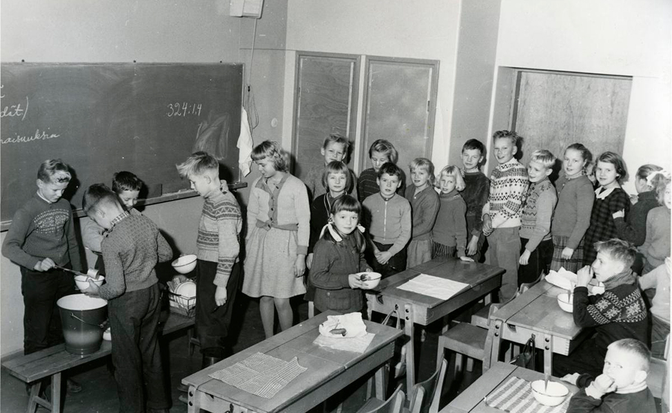 Rajamäen koulun oppilaat Nurmijärvellä jonottavat kouluruokaa. Kuva on otettu 1950- tai 1960-luvulla.