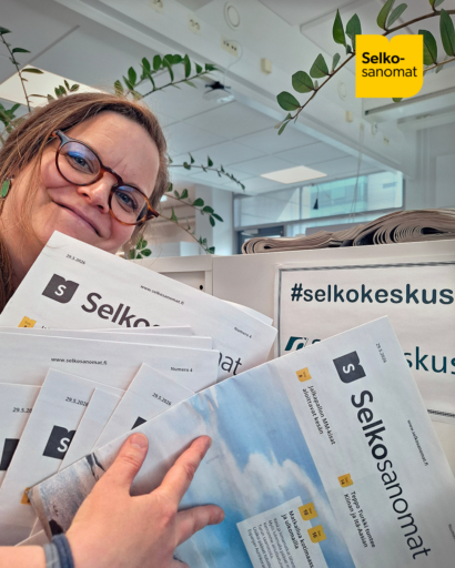 Toimittaja esittelee iloisena Selkosanomien uusinta numeroa. Hänellä on kädessään kasa lehtiä Selkokeskuksen toimistolla.